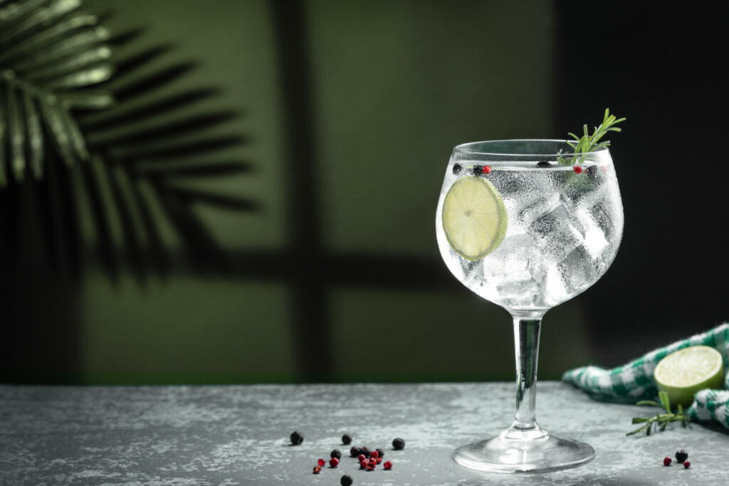 Gin tonic cocktail and shadows next to the window on dark concrete background.