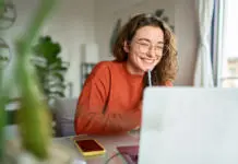 Prijavi se! Iščemo pisce člankov za portal student.si! Happy young woman using laptop sitting at desk writing notes while watching webinar, studying online, looking at pc screen learning web classes or having virtual call meeting remote working from home.