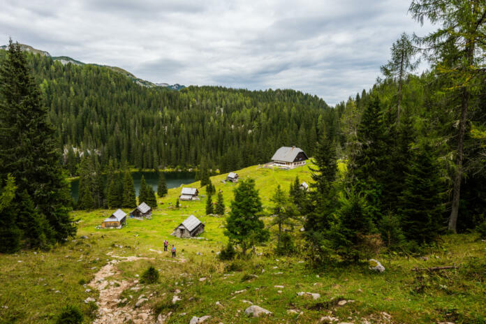 Log cabins and a mountain lake in the mountains of the Slovenian Alps on the peak Planina Blato on sunny day with clouds