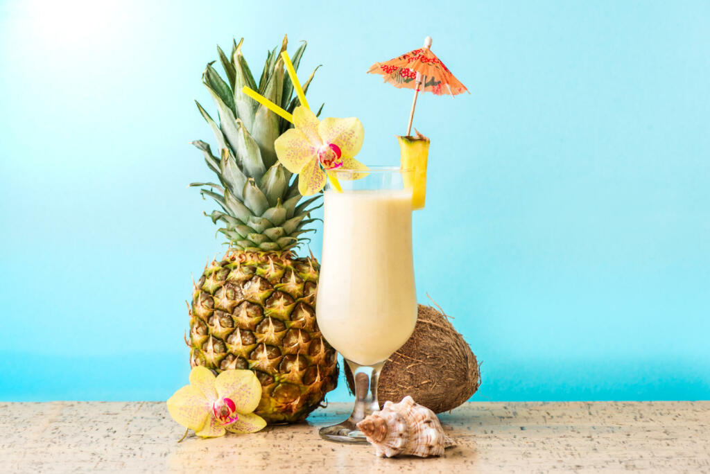 Pina Colada Cocktail Drink with pineapple and coconut, blue background, copy space. Summer tropical delicious cocktail with fruits and flowers, vacation concept.