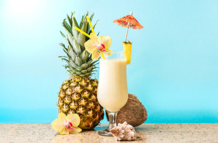 Pina Colada Cocktail Drink with pineapple and coconut, blue background, copy space. Summer tropical delicious cocktail with fruits and flowers, vacation concept.