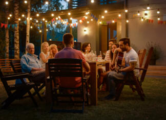 Tako boš ustvaril najbolj pristne in pomembne spomine Sitting at the Dinner Table Handsome Young Man Plays the Guitar For a Friends. Family and Friends Listening to Music at the Summer Evening Garden Party Celebration.