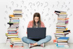 Woman using Laptop. Student Girl working on Computer Search in Internet around Stacks of Books. Question Marks Drawn On White Wall Background. E Learning, Online Studying, Reading Books in Digital Library. Young Girl sitting on Floor next to heap of Books