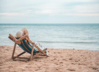 Študent priporoča: najboljše knjige za oddih na morju Beautiful young asian woman with hat arm up relaxing on beach chair, Summer happy beach vacation concept.