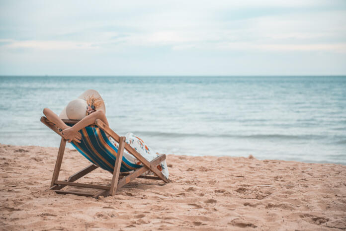 Beautiful young asian woman with hat arm up relaxing on beach chair, Summer happy beach vacation concept.