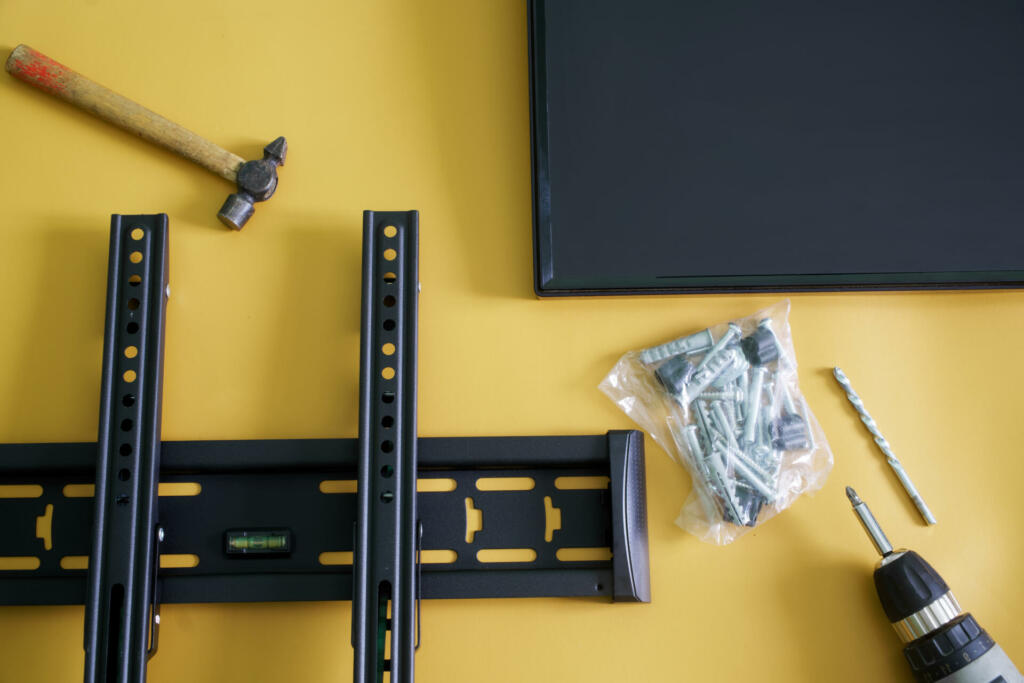 Bracket for wall mounting a computer monitor or TV, screwdriver, fasteners, hammer and monitor screen on a yellow background. Concept of wall mounting computer monitor or TV in the interior. Close-up