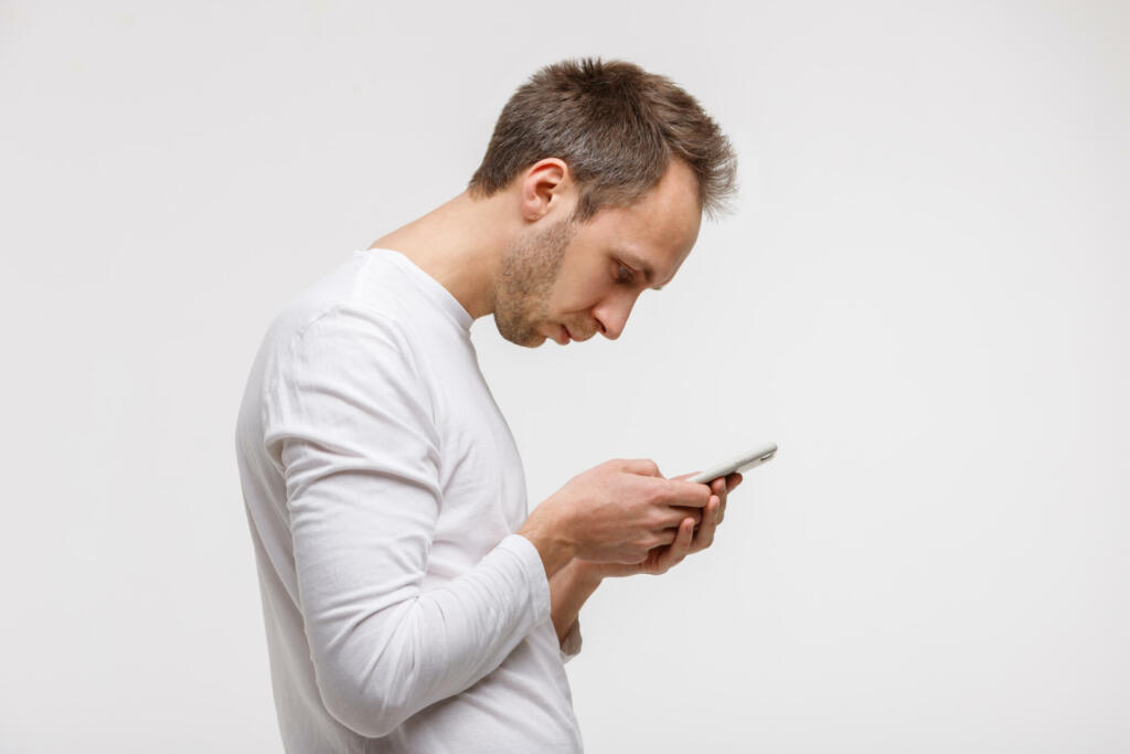 Close up portrait of man looking and using smart phone with scoliosis, side view, isolated on gray background. Rachiocampsis, kyphosis curvature of neck, Incorrect posture,orthopedics concept