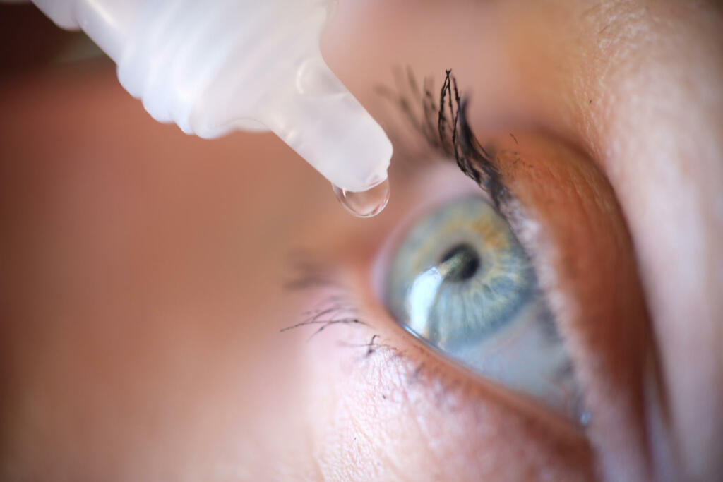 Drops from vial dripping into woman eye closeup. Conjunctivitis treatment concept