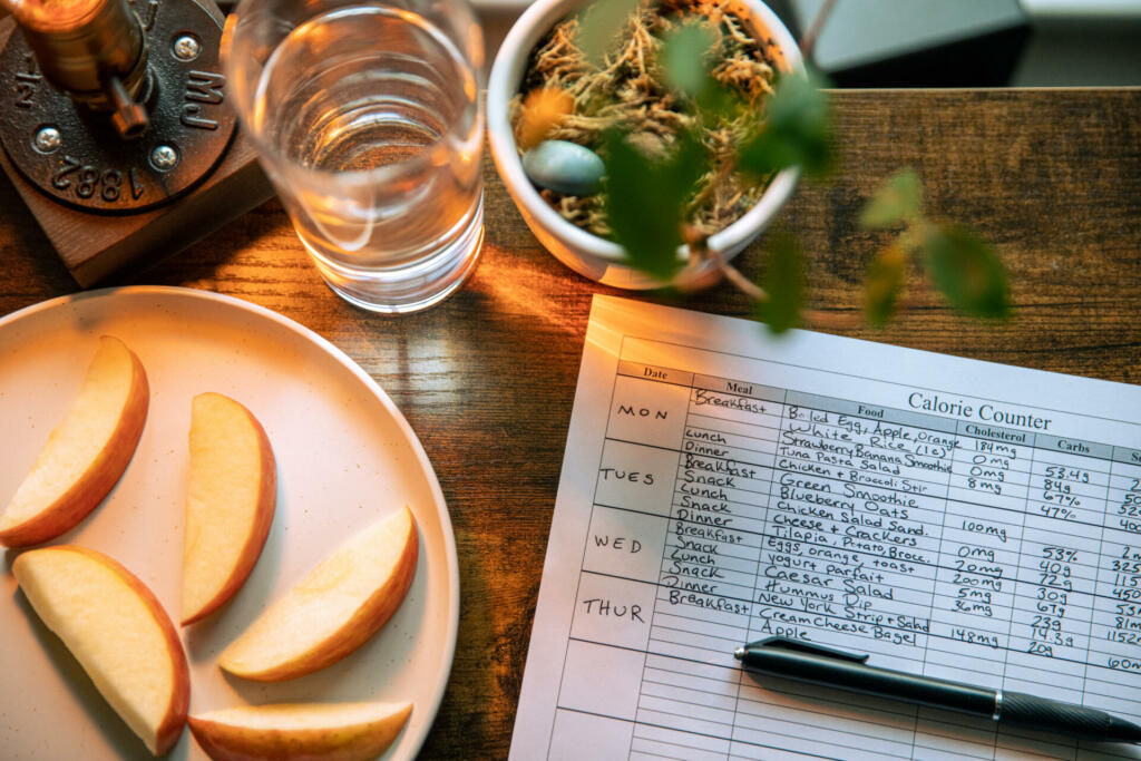 Glass of water beside slices of apple and record on calorie count on brown wooden table