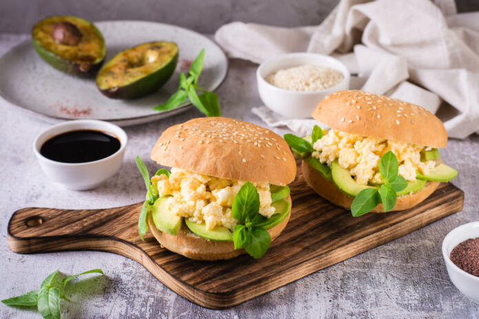 Hamburger with avocado, scrambled eggs and basil on a board on the table. Healthy food.