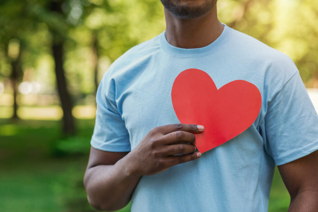 Love, volunteering and charity concept, copy space. Young black man holding red heart on his chest.