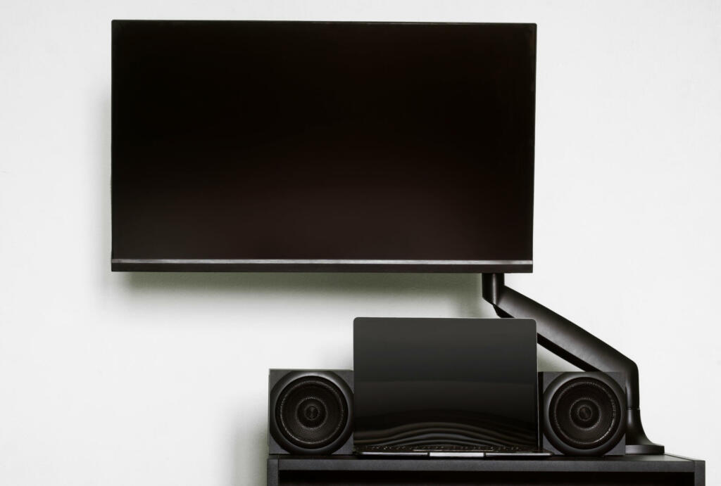 Modern computer monitor is mounted on a small table, along with audio speakers and a laptop, using a gas-lift metal bracket. Off-center side holder. Designer's workplace. Light background