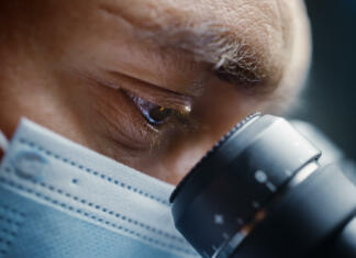 Človeštvo je korak bližje vrelcu mladosti, menijo znanstveniki Ultra Macro Close Up Shot of a Male Scientist Wearing Surgical Mask and Looking into the Microscope. Microbiologist Working on Molecule Samples in Modern Laboratory with Technological Equipment.