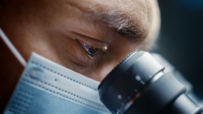 Ultra Macro Close Up Shot of a Male Scientist Wearing Surgical Mask and Looking into the Microscope. Microbiologist Working on Molecule Samples in Modern Laboratory with Technological Equipment.