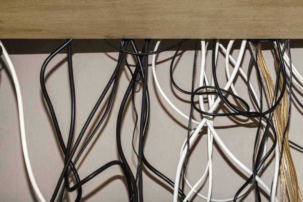 Untidy cables hanging behind a computer desk. Various colors and types of cables hanging loose and tangled without cable management.