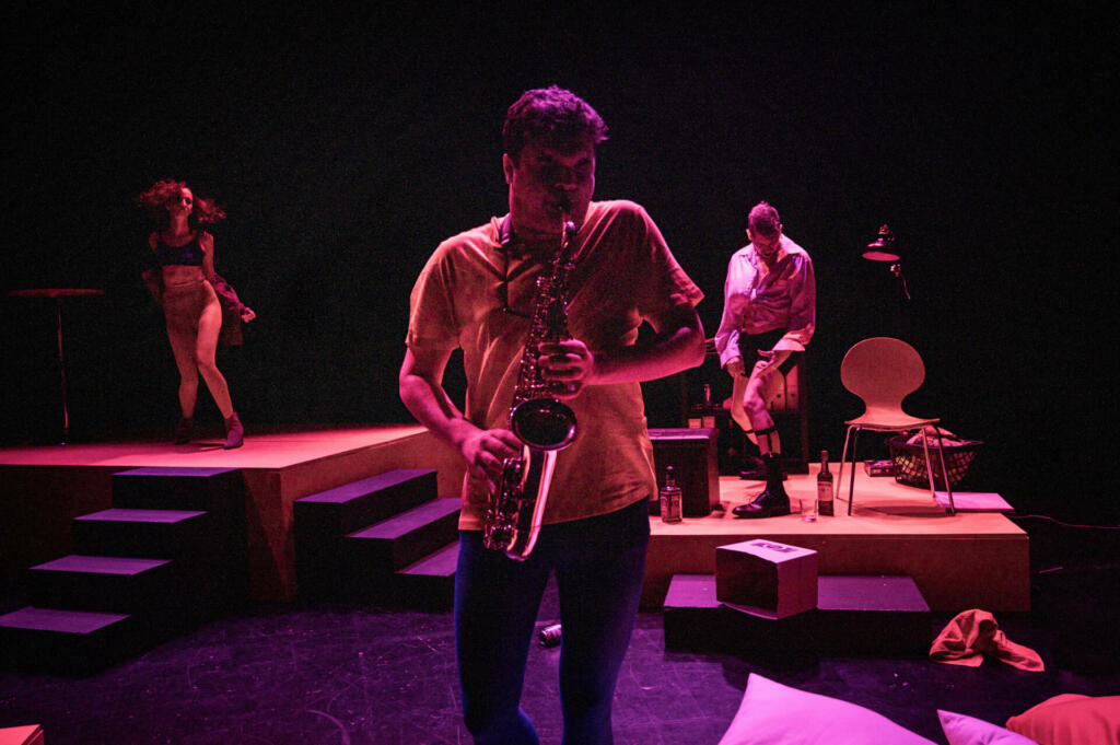 Moški igra na saksofon, v ozadju plešeta fant in punca