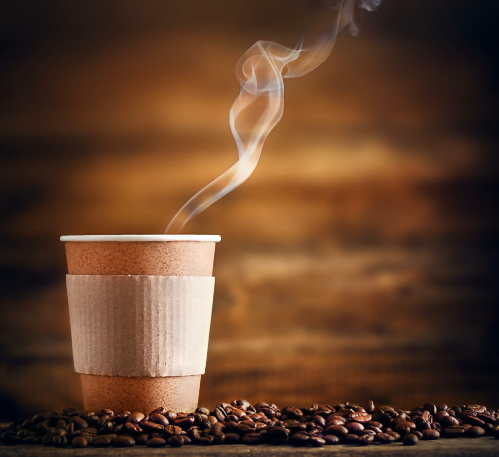 a paper cup with a hot drink stands on coffee beans on a wooden background