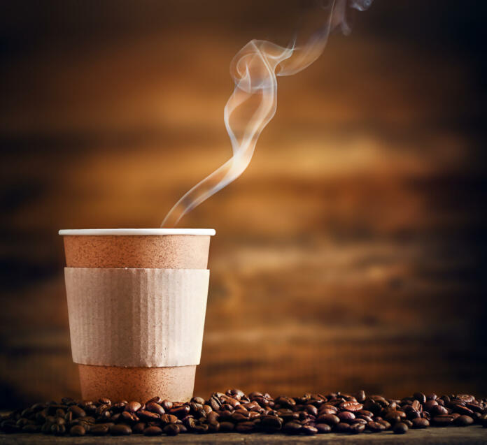 a paper cup with a hot drink stands on coffee beans on a wooden background
