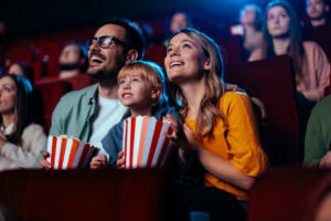 A young joyful couple is with their daughter in the cinema, watching an exciting movie.