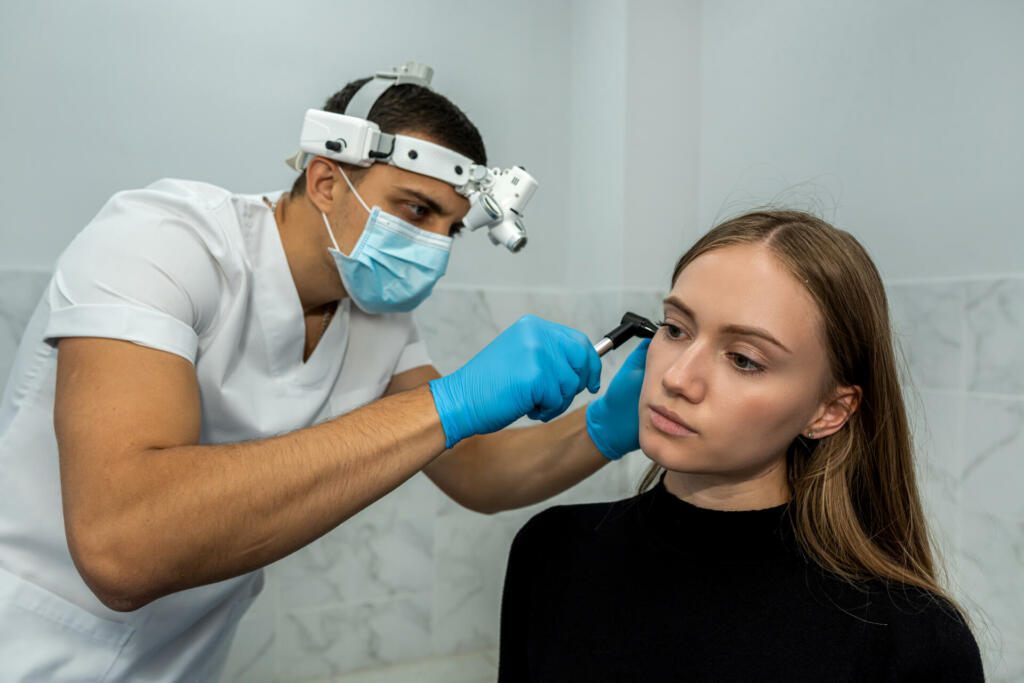 An otolaryngologist examines the auricle. Hearing clinic. An ENT doctor with instruments in a mask and gloves examines the patient's ear.