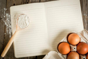 Baking background. Tools and ingredients for baking on the old rustic wooden table. Book notepad for recipes. Top view copy space