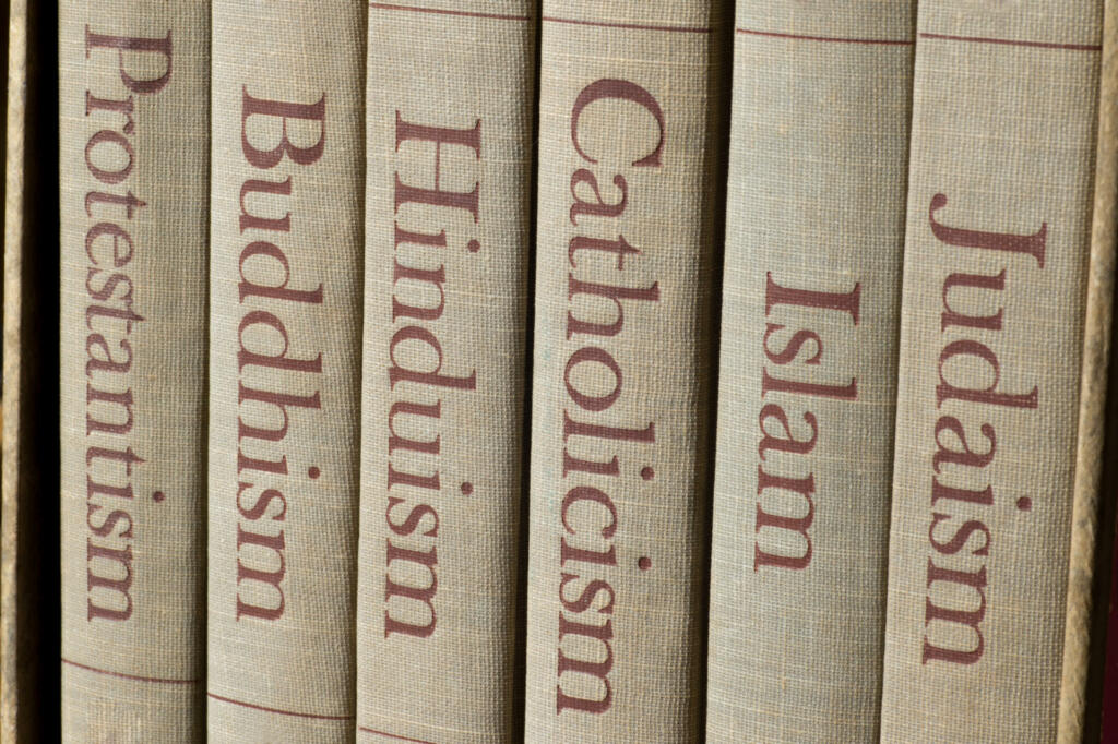 Book spines listing major world religions - Judaism, Islam, Catholicism, Hinduism, Buddhism and Protestantism.