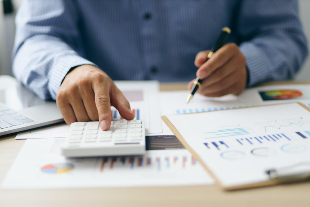 Businessman using a calculator to calculate numbers on a company's financial documents, analyzing historical financial data to investment planning in the future. Finance and Accounting Concepts