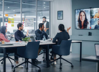 Ironija: Direktor Zooma je naveličan Zooma Businesspeople do Video Conference Call with Big Wall TV in Office Meeting Room. Diverse Team of Creative Entrepreneurs at Big Table have Discussion. Specialists work in Digital e-Commerce Startup