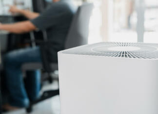 Zakaj študent nujno rabi čistilec zraka? Close up Air purifier in the room is very safe and clean to breathe with filter dust PM 2.5 and a man use computer desktop working in home in clean air