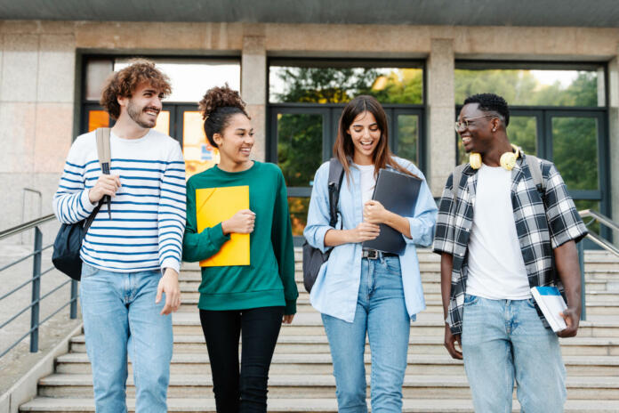 Happy students walking together on university campus, chatting and laughing outdoors after classes