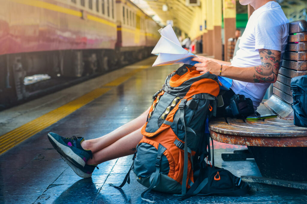 Man holding a map with backpack, camera and a smart phone in a train station