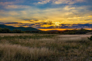 Sunrise coming over mountains behind a field of tall grass taken on the last day before the time changed in the Texas Hill Country