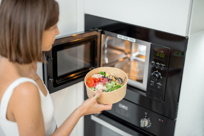 Woman heating food with microwave machine at home, female using modern kitchen appliances