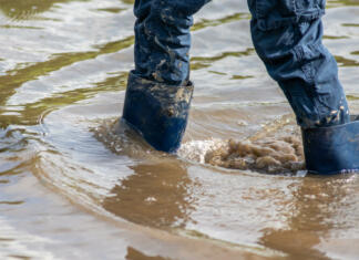 Po poplavi – čustvena stiska in kako jo obvladati Young boy with short blue trowsers wading with wet socks and wet boots through high tide after a floodwater has broken the dike and overflown the lands behind