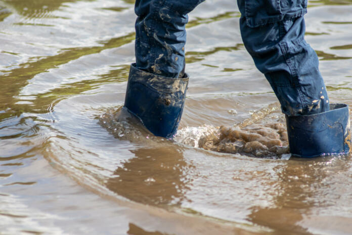 Young boy with short blue trowsers wading with wet socks and wet boots through high tide after a floodwater has broken the dike and overflown the lands behind