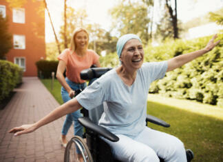 Obetavni rezultati zdravljenja raka prihajajo iz Švice A woman with cancer is sitting in a wheelchair. She walks on the street with her daughter and they fool around. They are fun and they laugh. They walk in the courtyard of the clinic.