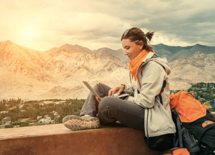 Backpacker with laptop sits on the top view point under mountain settelment