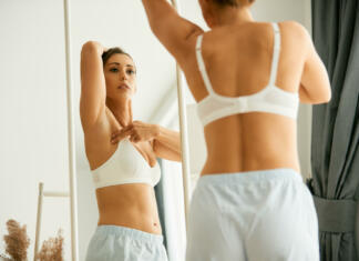 Kako poteka samopregled dojk? Cancer aware young woman looking herself in a mirror while doing breast self-examination at home.