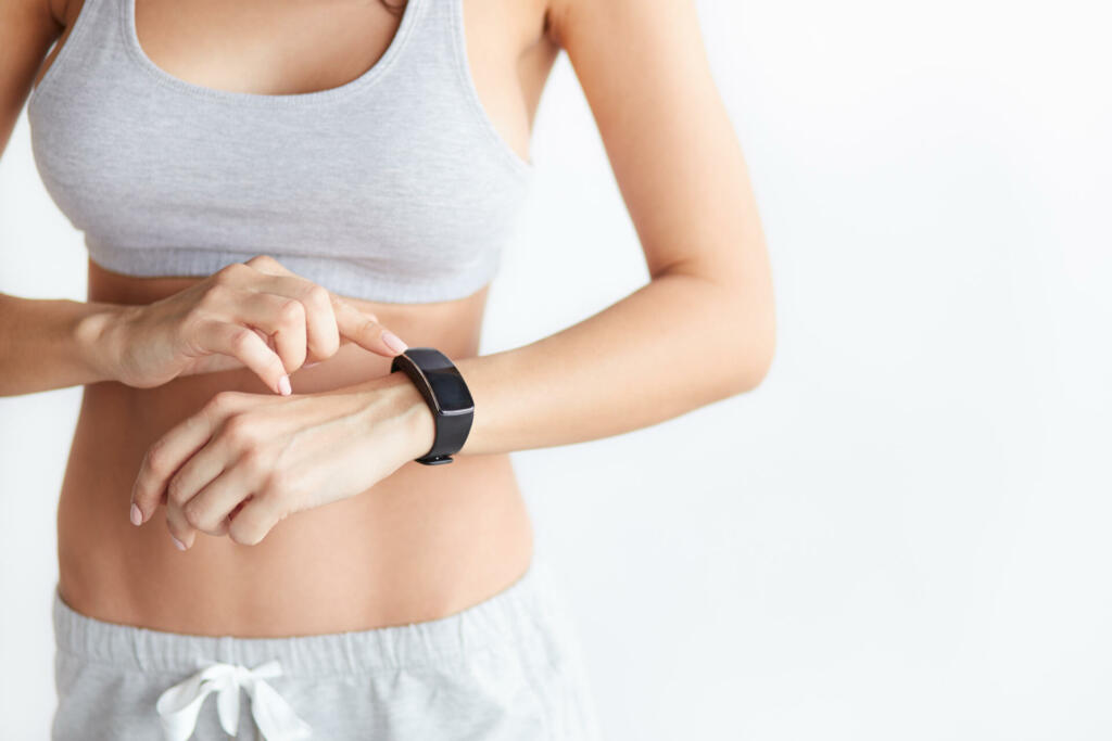 Closeup activity tracker on a woman's wrist on white background. Fitness girl touching her smart watch. Focus on hands