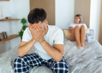 Od zmenka do urgence: Kaj vse lahko gre narobe? Sad thoughtful man after arguing with girlfriend.Relationship difficulties, conflict and family concept,unhappy couple having problems at bedroom. Sad guy sitting on bed,girlfriend in the background