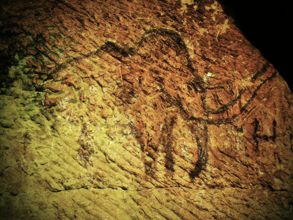 Abstract children art in sandstone cave. Black carbon mammut paint of human hunting on sandstone wall, copy of prehistoric picture.