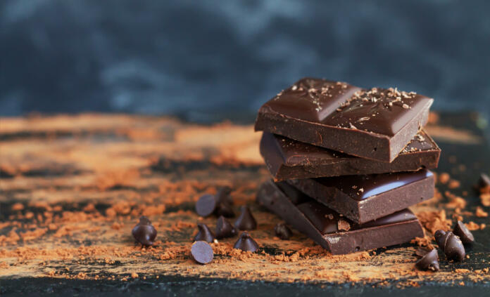 Bitter chocolate stack with chocolate flakes, drops and cocoa powder on dark background