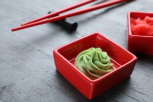 Bowls with swirl of wasabi paste and pickled ginger on grey table, closeup
