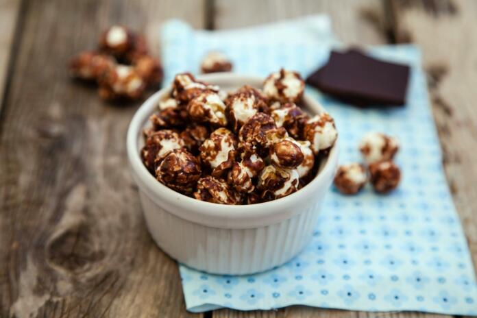 Chocolate covered popcorn in a white bowl on wooden table