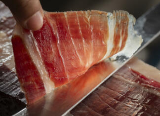 Zakaj je španski pršut najboljši na svetu? Close up view of a slice of Iberian ham cut with a knife by a professional. Concept Iberian ham from Spain with denomination of origin.