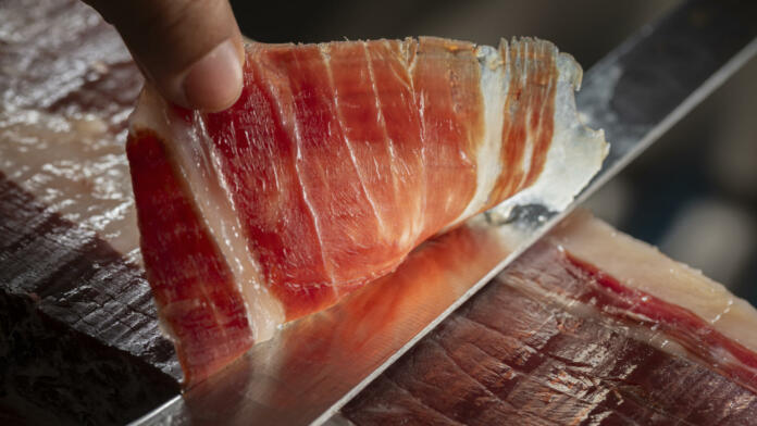 Close up view of a slice of Iberian ham cut with a knife by a professional. Concept Iberian ham from Spain with denomination of origin.