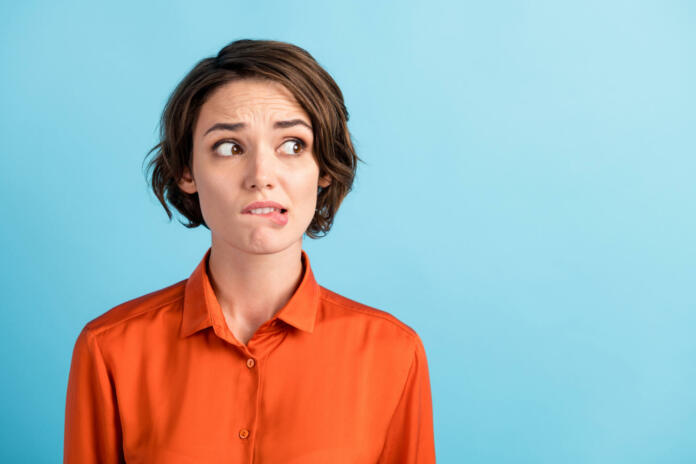 Closeup photo of sad depressed displeased lady horrified facial expression, made huge big mistake feel guilty look side empty space bite lips wear orange shirt isolated blue color background