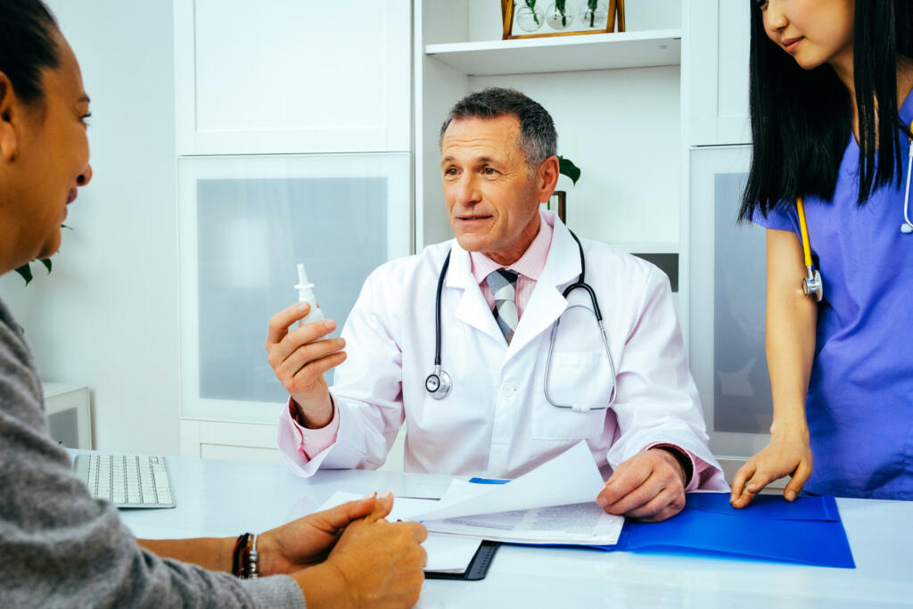 doctor physician and nurse practitioner giving nasal spray to female patient in hospital consultation healthcare industry