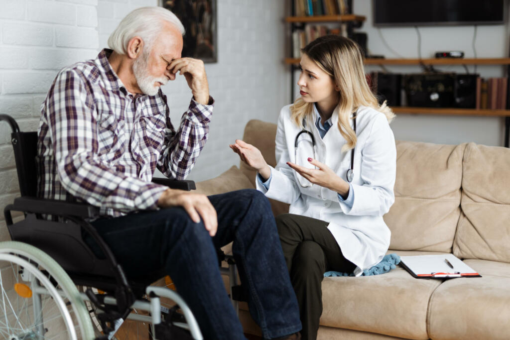 Female nurse talking with mature man in a wheelchair during home visit