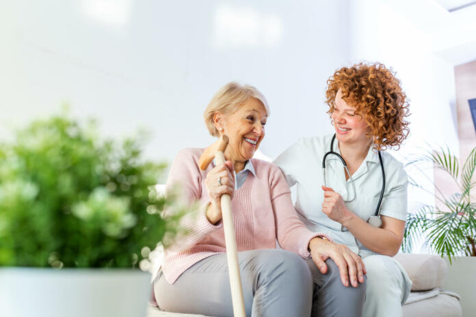 Friendly relationship between smiling caregiver in uniform and happy elderly woman. Supportive young nurse looking at senior woman. Young caring lovely caregiver and happy ward